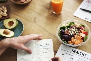 O masă cu un bol de salată și o persoană care scrie un plan de dietă