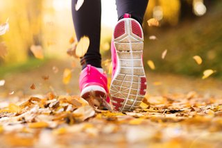 Prim-plan al pantofilor de alergare roz al unui alergător, în frunze de toamnă pe pământ