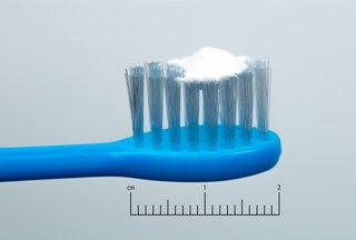 fotografie cu o periuță de dinți albastră a unui copil cu o cantitate de pastă de dinți de dimensiuni de mazăre lângă o scară de 2 cm