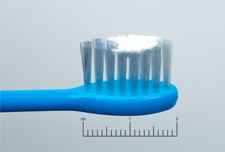 fotografie cu o periuță de dinți albastră a unui copil cu un frotiu de pastă de dinți lângă o scară de 2 cm