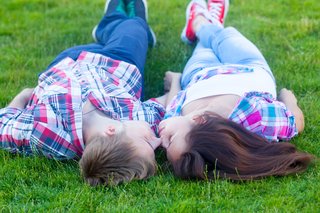 Un băiat și o fată adolescentă întinsă pe iarbă, atingându-și ușor nasurile